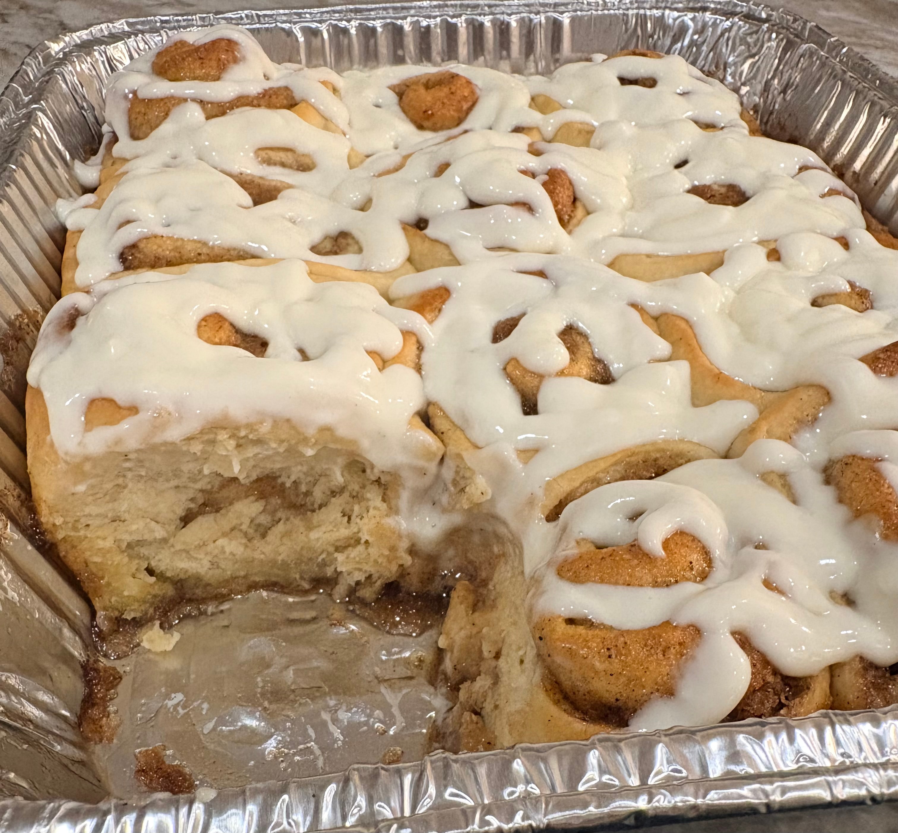 Freshly baked cinnamon rolls with cream cheese icing in a catering tray